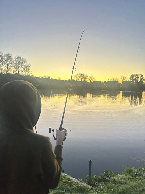 Person fishing by a calm lake during sunset.