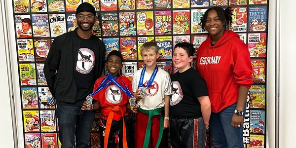 Group photo of kids with medals and adults in front of a cereal box wall.