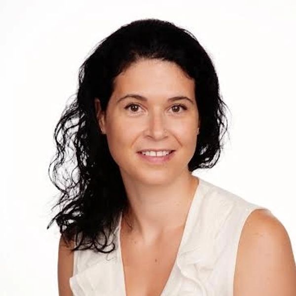 Femme souriante aux cheveux noirs ondulés, en chemisier blanc.