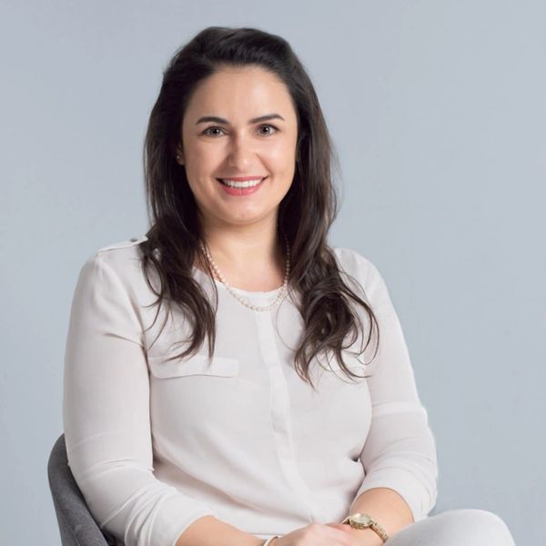Femme souriante en chemise blanche assise sur une chaise.