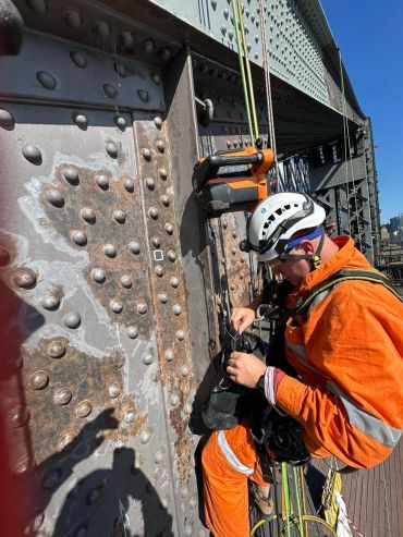 Worker in safety gear inspecting a rusted metal bridge.