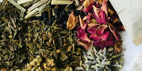 Dried herbs and flowers surrounded by tea bags on a white surface.
