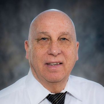 Portrait of an older bald man in a white shirt and striped tie.