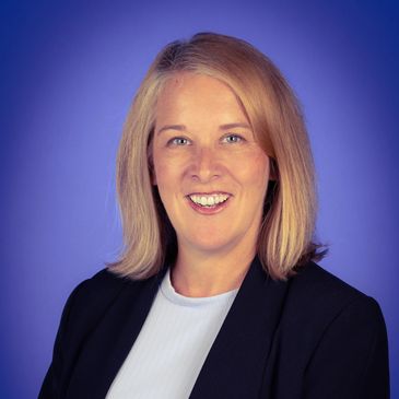 Smiling woman in professional attire against blue background.