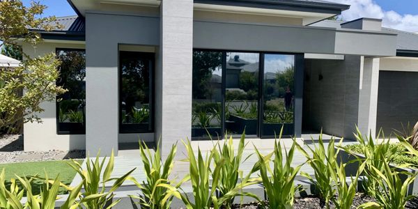 Modern house exterior with large windows and lush green plants.
