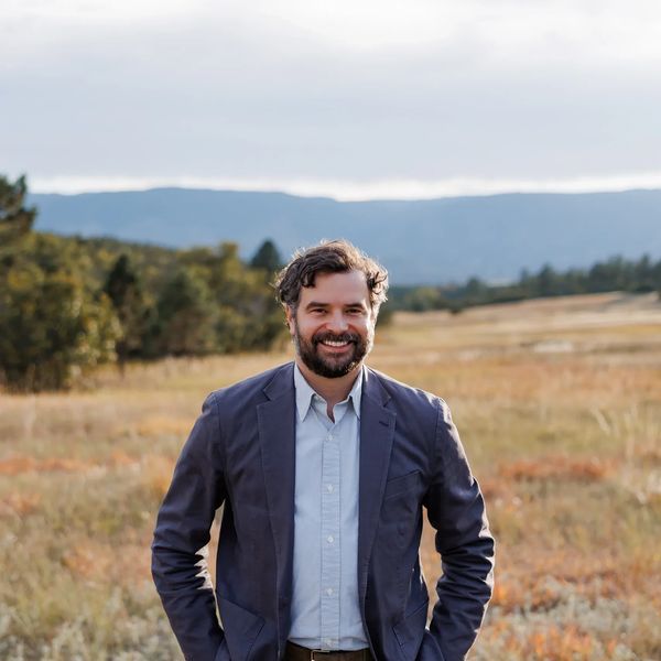 Smiling man in a blazer standing in a scenic outdoor field.