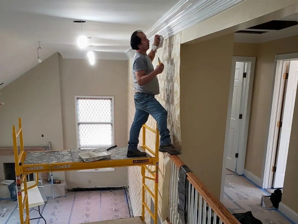 Man precariously standing on scaffolding and railing applying wallpaper.