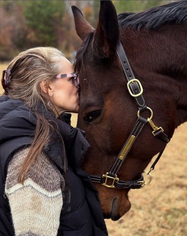 A woman tenderly kisses a horse on the forehead outdoors.