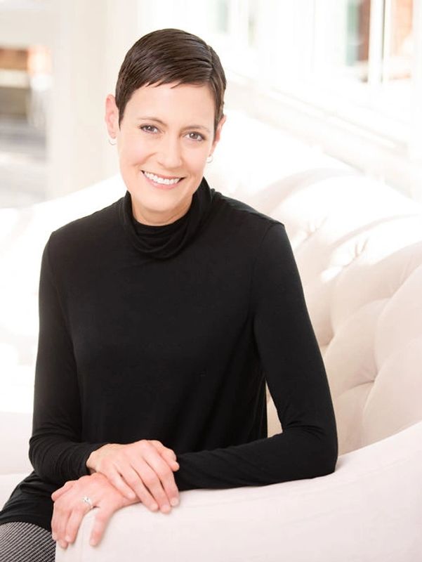 Smiling woman in black turtleneck sitting on a white sofa.