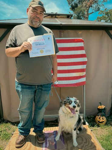 Man holding a K9 training certificate with his dog beside him outdoors.