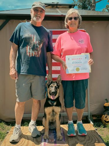 Two adults with a German Shepherd dog holding a K9 training certificate.