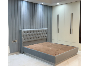 Modern bedroom with grey upholstered bed and white wardrobe.