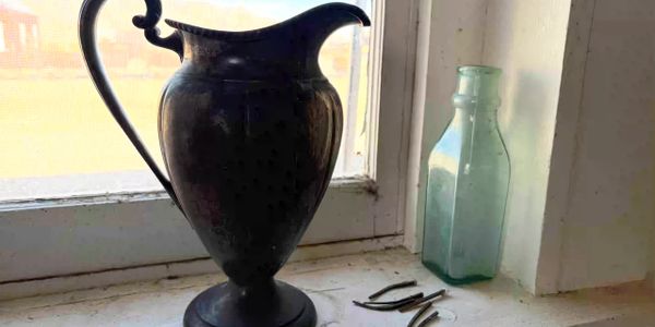 Rusted metal axle on narrow-gauge rail—remnants of a mine cart. Behind is a vintage metal lantern.