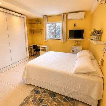Bright yellow bedroom with white bed, desk, TV, and geometric rug.