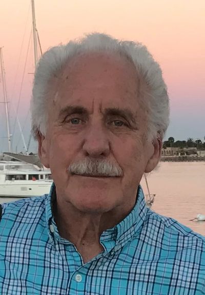 Elderly man outdoors with boats in the background at sunset.