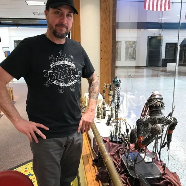Man standing next to intricate metal sculptures in a display case.