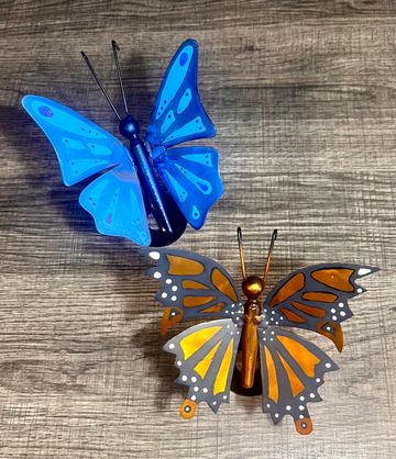 Two colorful decorative butterflies on a wooden surface.