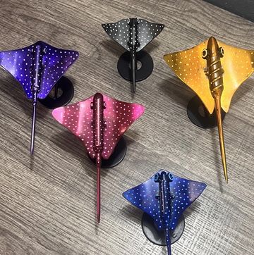 Five colorful spotted stingray models on black stands.