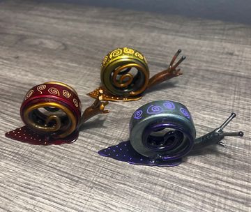 Three colorful metallic snail figurines on a wooden surface.