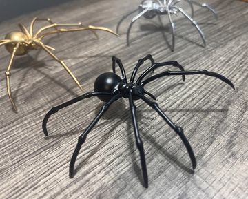 Three metallic spider sculptures on a wooden surface.