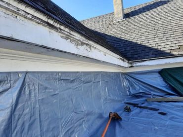 Roof corner with blue tarp and tools under clear sky.
