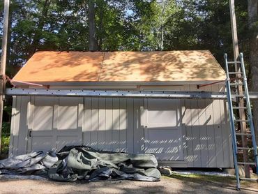 A shed with a newly installed wooden roof under construction in a wooded area.