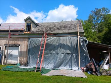 Old house undergoing roof repairs with ladders and tarps in place.