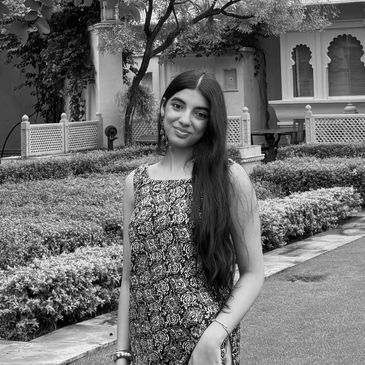 Young woman smiling in a garden with lush greenery and traditional architecture.