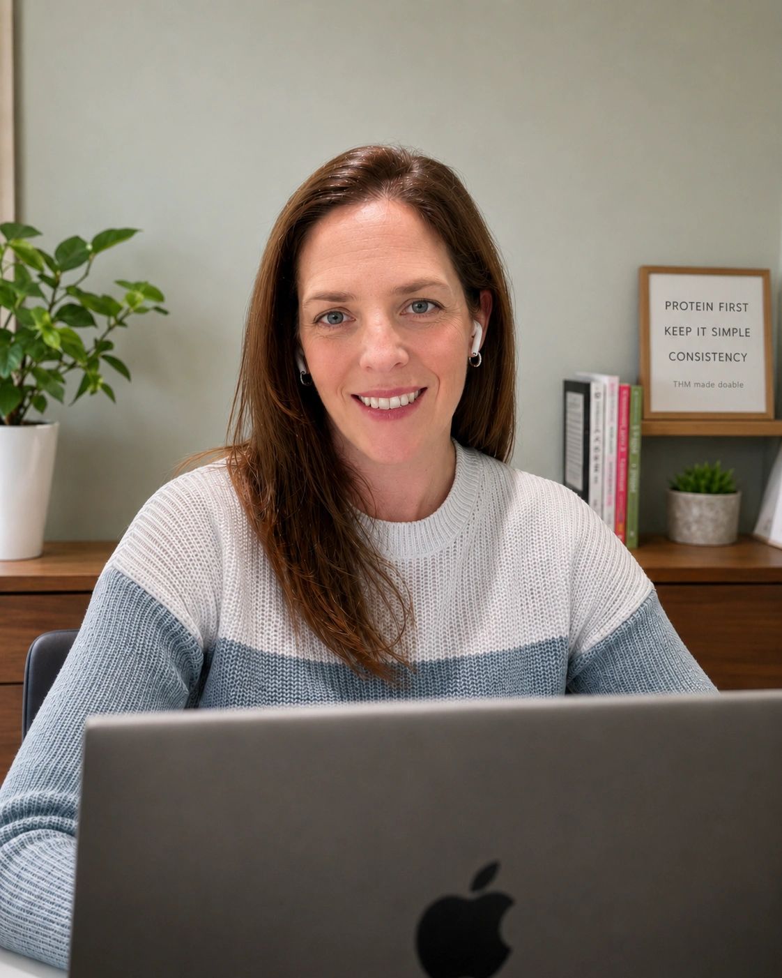Woman smiling while working on a laptop in a cozy home office.