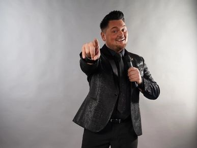 Man in a black suit pointing forward with a microphone.