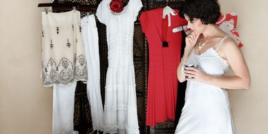 A woman in a white dress considers options from several dresses hanging on a rack.