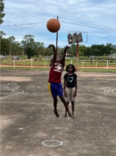 Two children playing basketball outdoors on a concrete court.
