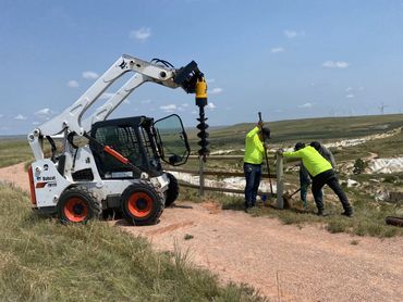 Contract Equipment Operators crew drilling fence post holes with skid steer auger in Wyoming