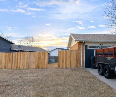 Completed wood privacy fence installation by Contract Equipment Operators with company trailer on si