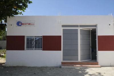 Fachada de un pequeño edificio blanco con puerta gris abierta.