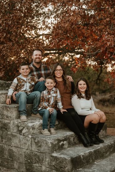Family portrait on stone steps with autumn leaves in background.