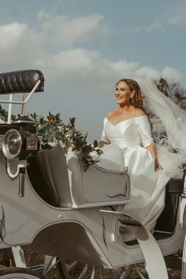 A joyful bride in a white gown sitting in a decorated horse carriage.