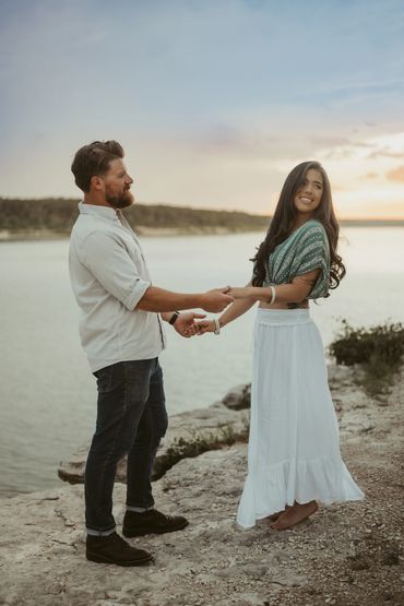 A couple holding hands by a lakeside at sunset.