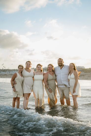 A happy group of six friends or family standing in the ocean water at sunset.