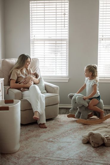 Mother holding a baby while older child plays on a rocking elephant toy.