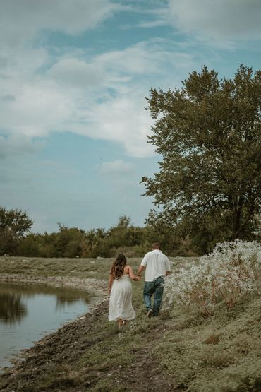 Couple holding hands while walking by a lakeside on a cloudy day.