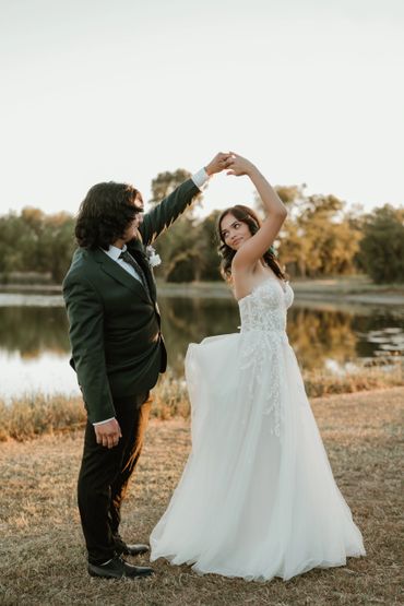 Bride and groom dancing by a lakeside at sunset.