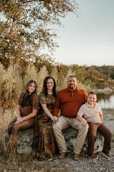 A family of four posing outdoors on a rock by a lake.