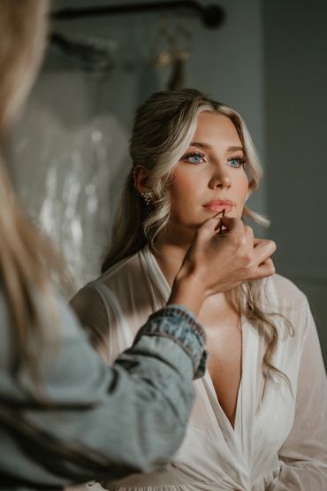 A woman with blonde hair gets lip makeup applied before a special event.