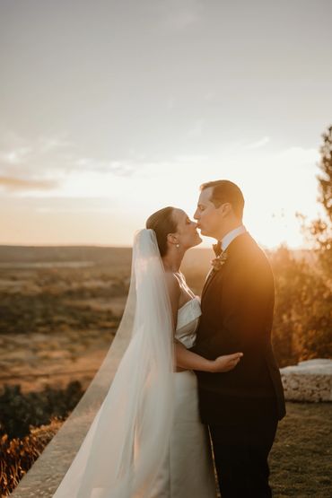 Bride and groom share a kiss at sunset during their wedding.