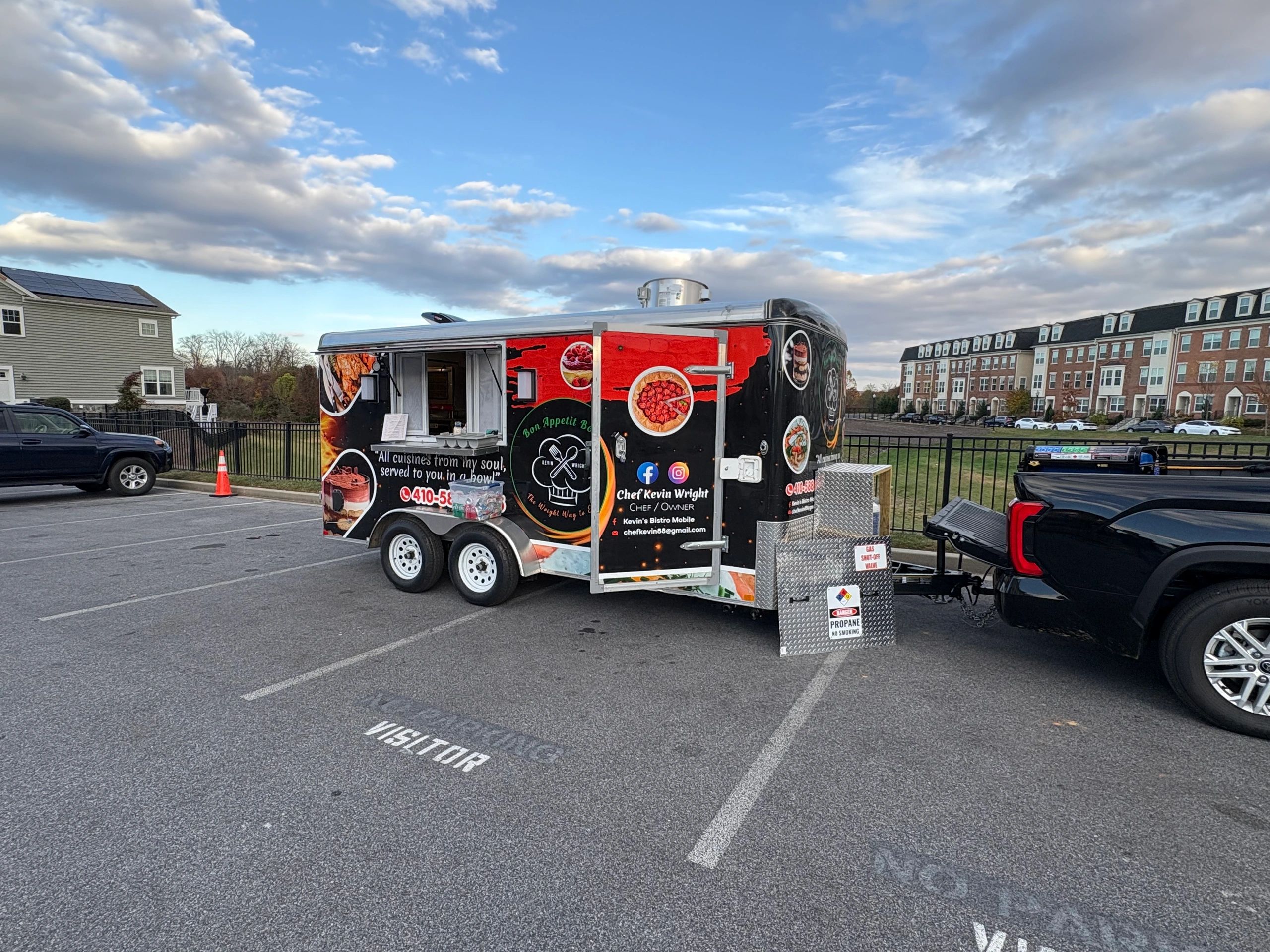 Food truck trailer parked in a visitor parking lot with a partly cloudy sky.