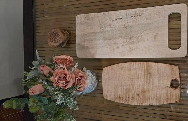Wooden cutting boards and a vase with artificial roses on a bamboo table.