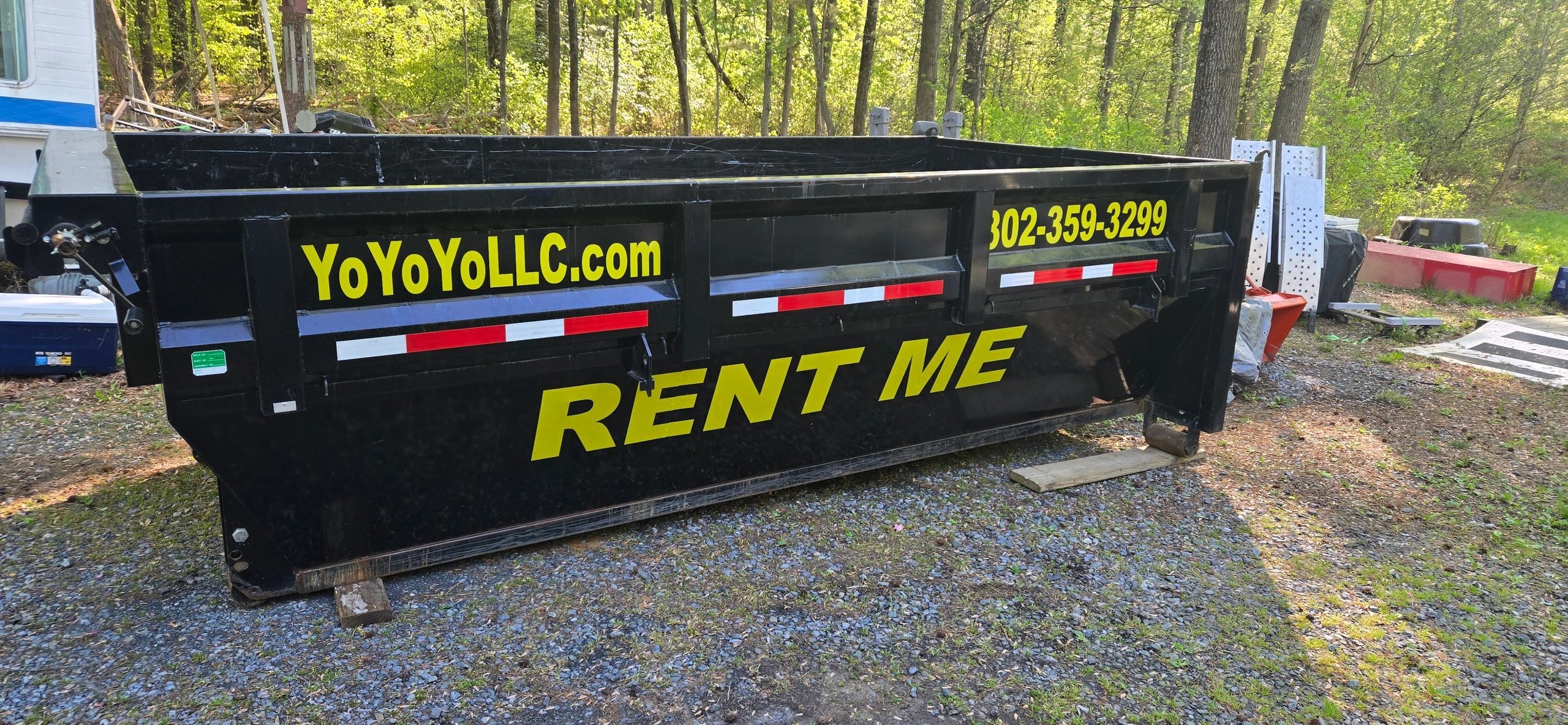 Black rental dumpster with yellow text and contact info outdoors.