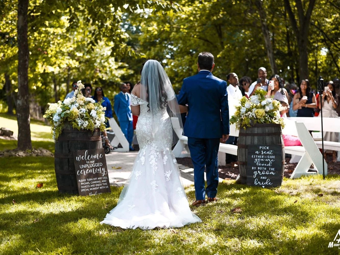 Father of the Bride and bride walking into outside wooded wedding ceremony wooden barrels flowers