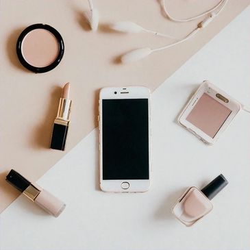 Flat lay of makeup items and smartphone on a beige and white background.